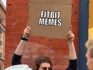 Person holding a cardboard sign labeled 'Fitbit Memes' while wearing a Fitbit wristband, humorously highlighting motivational struggles with workouts.