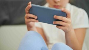 A child in a white shirt is holding a smartphone with both hands playing on speech apps.