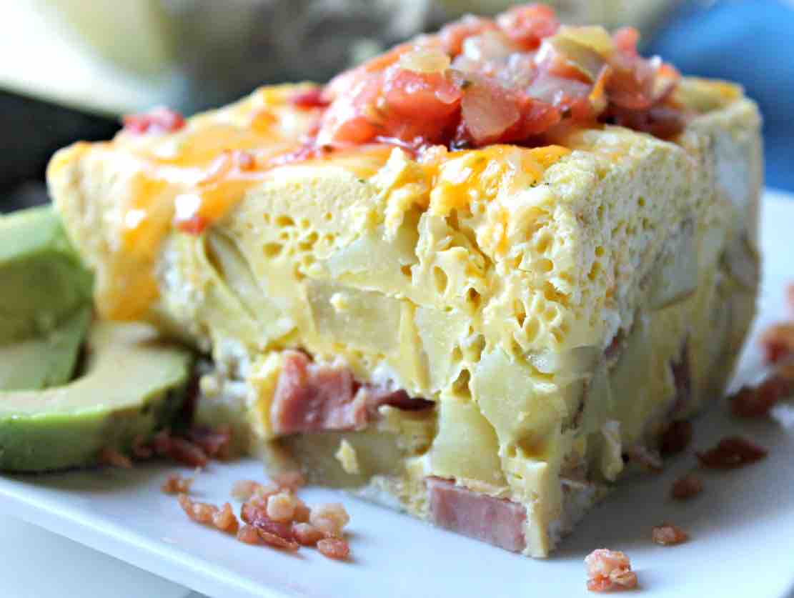 Instant Pot Egg Casserole six sisters A scrumptious breakfast casserole overflowing with eggs, cheese, and slices of ham, topped with juicy tomato bits, sitting beside a smug-looking avocado slice, all ready to make your taste buds tango.