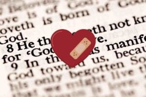 Meme featuring a heart with a bandaid overlayed on a zoomedin Bible page focusing on 1 John 4:8, illustrating 'He that loveth not knoweth not God; for God is love.'