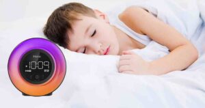 A child sleeps peacefully in bed next to an iHome alarm clock displaying the time as 10:09, with a colorful LED ring surrounding the display.