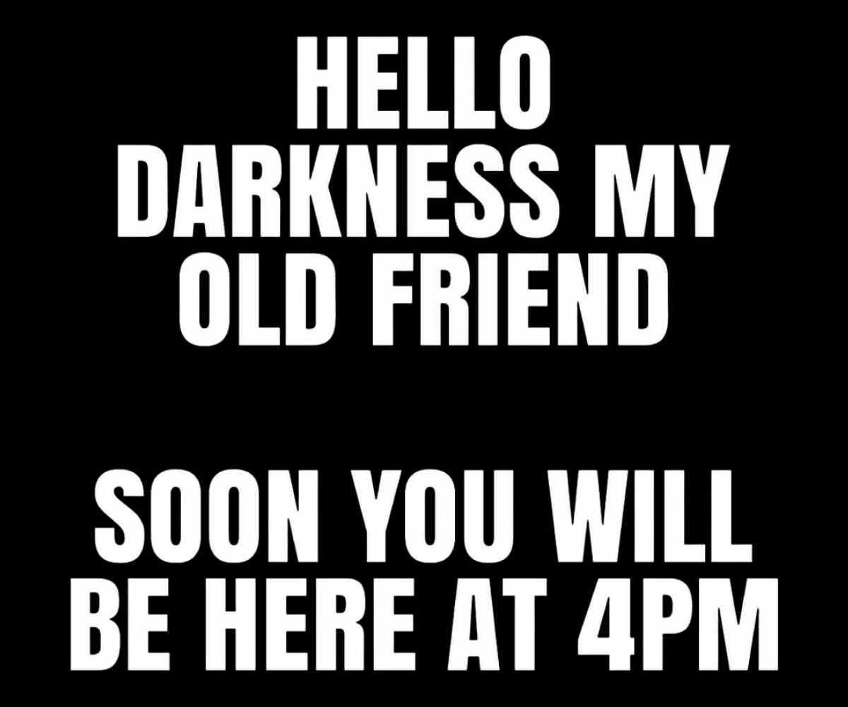 daylight savings fall back meme Daylight savings meme that humorously says, 'Hello darkness my old friend, soon you will be here at 4PM,' in bold white text on a black background, poking fun at early sunsets.