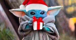 Baby Yoda wearing a Santa hat, holding a gift, looking festive and cute in this Christmas meme.