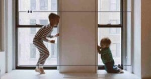 Meme featuring two children playing by a window, with a humorous quote above them.