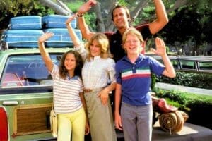 Family posing excitedly in front of a fully packed station wagon, ready for a road trip adventure, embodying classic summer vacation meme vibes.