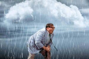 Funny meme of a man in glasses and a checkered jacket caught in a rainstorm, dramatically holding his stomach, embodying the mood of 'when you realize you left the windows open.'