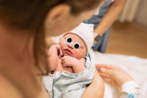 Meme of a newborn baby with googly eyes gazing curiously, as a parent holds them, humorously capturing the wideeyed wonder of realizing parenting just got real.