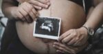 Pregnant person holding an ultrasound image against their bare belly in pregnancy announcement memes.