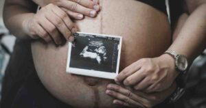 Pregnant person holding an ultrasound image against their bare belly in pregnancy announcement memes.