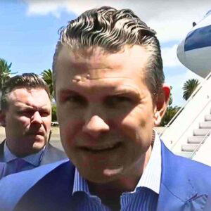pete hegseth meme generator template Two men in suits stand outdoors with the focus on Pete Hegseth in front, who has slickedback hair and a blue suit, against the backdrop of an airplane staircase and palm trees.