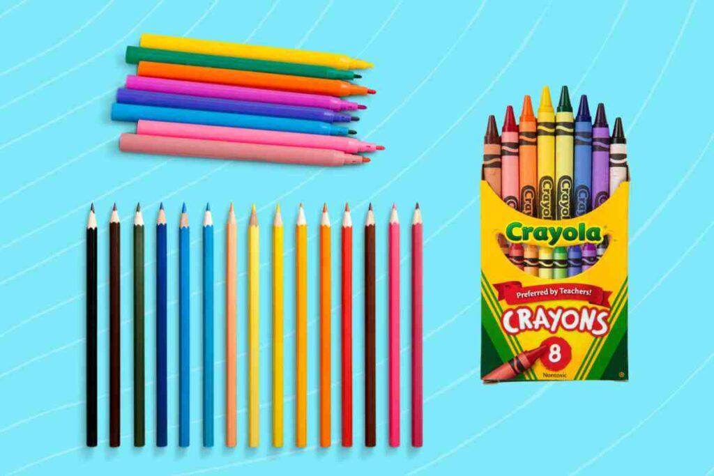 coloring unicorn supplies A variety of colored pencils, pens, and an open box of Crayola crayons arranged on a light blue background with subtle streaks. The items are neatly organized with the pencils and pens laying parallel to each other and the crayon box standing upright, displaying its contents.