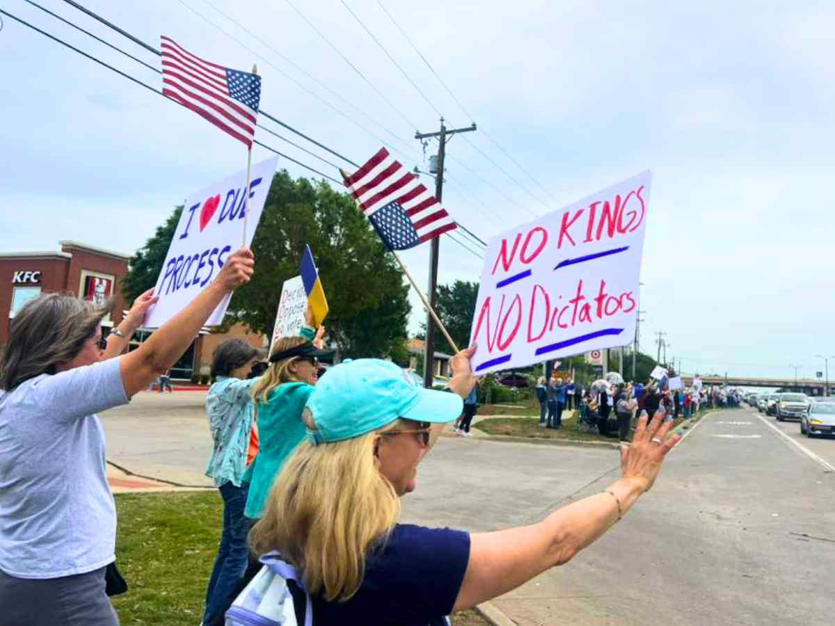 no kings protest A group of protesters holding signs and American flags in a street demonstration, with messages like "I ❤️ Due Process" and "No Kings, No Dictators."